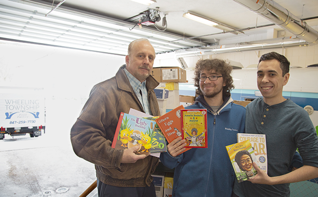 A library employee and two Wheeling Township employees stand in front of 40+ boxes of donated books.