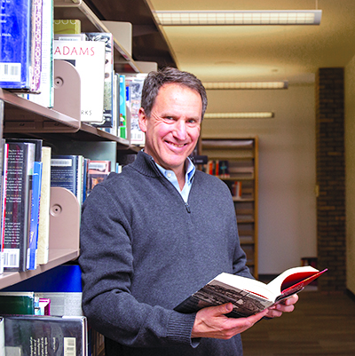 Customer Ken Nopar holding an open book in the library's shelving area