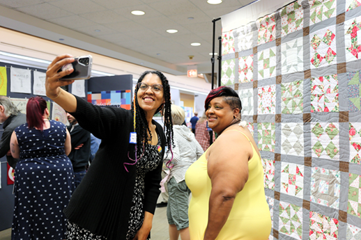 Two women stand in front of Freedom Quilt and smile while taking a selfie.
