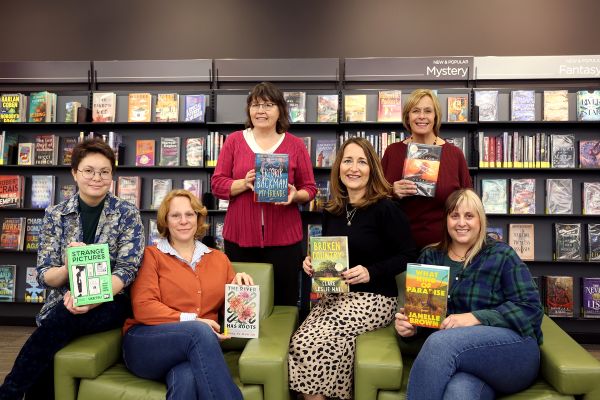 Info Advisors sitting in the New and Popular Section of the library holding their favorite books of 2025